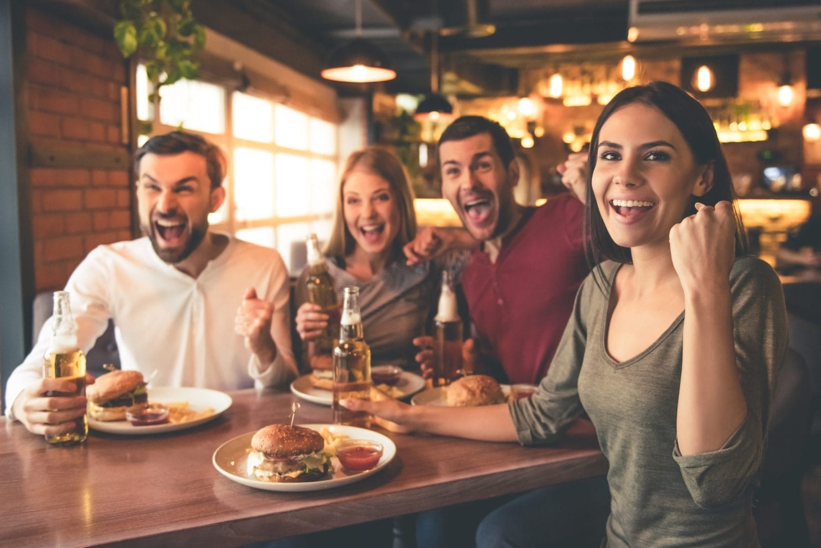 Four people sitting at a sports bar with burgers and beers