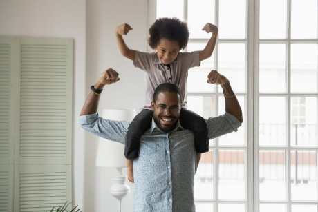 Son on fathers shoulders flexing muscles