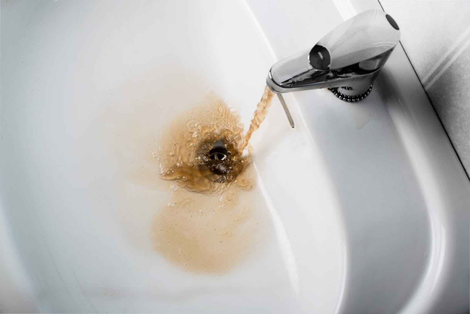 Dirty brown water running into a white sink